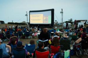 Screen on the Green. A photo of people sitting in chairs in front of a big screen on Littlehampton East Green.