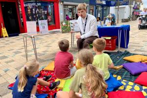 Summer Hight Street Event, week 2. A man is talking to the children sitting on the blankets.