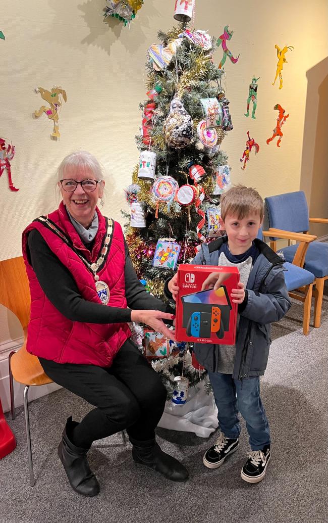 12 Days of Christmas winner Theodore Baker receiving prize from Town Mayor Councillor Jill Long in front of a Christmas Tree