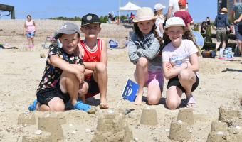 Sandcastle Competition 2024 children sitting on the beach with sandcastles