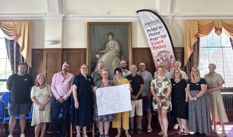 Group photograph of the Pride in Place Wick and Toddington Neighbourhood Board and project team standing together in the Littlehampton Town Council's Chamber, holding a map of the proposed Pride in Place neighbourhood boundary beside a Pride in Place event banner
