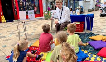 Summer Hight Street Event, week 2. A man is talking to the children sitting on the blankets.